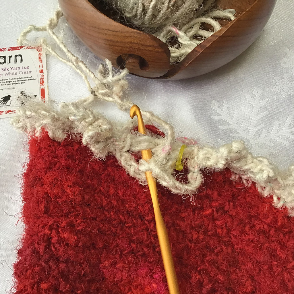 Yellow Crochet Hook with red and white yarn crochet project, a wooden yarn bowl, and white ball of yarn on a white background