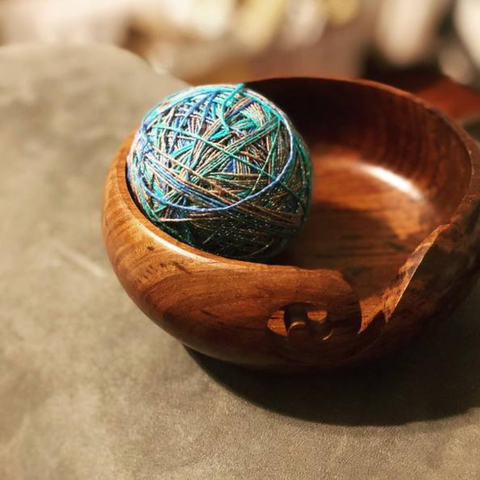 A ball of blue and tan sparkly lace weight silk yarn is resting in a wooden yarn bowl.
