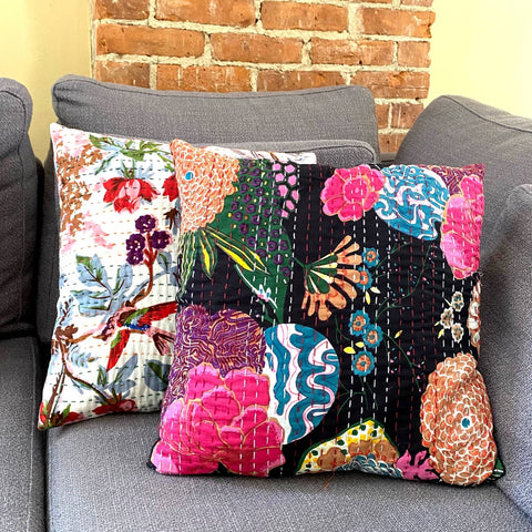 Two kantha pillows, one white and one black, are sitting on a light grey couch.