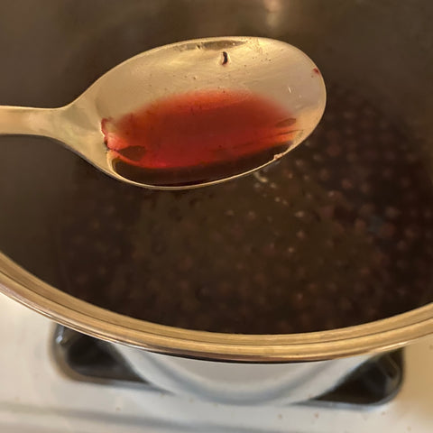 The pot filled with blueberries is simmering away on the stove. Closer to the camera is a large tablespoon filled with the dye, which is a deep violet.