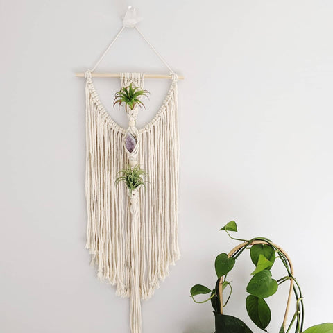 A handmade macrame kit is hanging off a white wall.