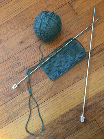 green yarn ball, silver aluminum knitting needles, and a matching knit project on a wooden surface