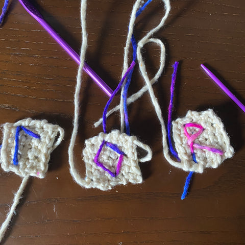 Three different unfinished runes made of white and multicolored yarn are laying on a dark wooden table.