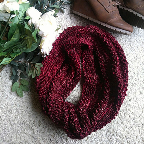 A cowl made of deep red yarn is laying on a white carpet.