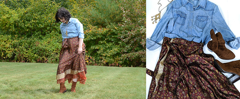 women wearing denim shirt tucked into a red and copper sari wrap skirt with a long necklace and brown sock boots standing in grass