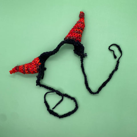 A pair of black and red crochet devil horns are curled up creepily on a green background.