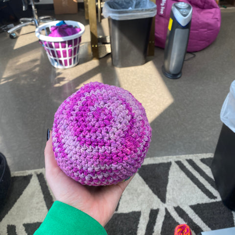 A hand outstretched, holding a large amigurumi circle made of sparkly ombre pink yarn.
