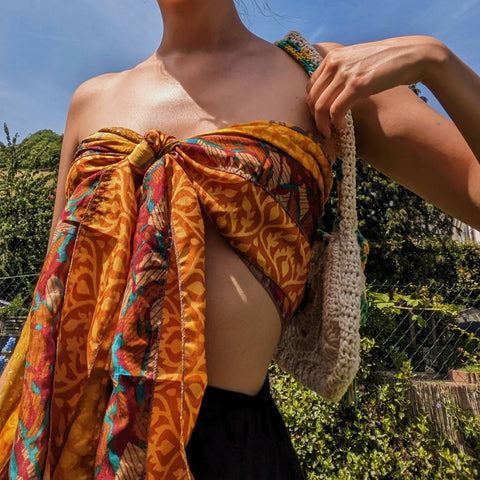 A woman from the neck down, a red and yellow scarf wrapped around their torso into a bow top.