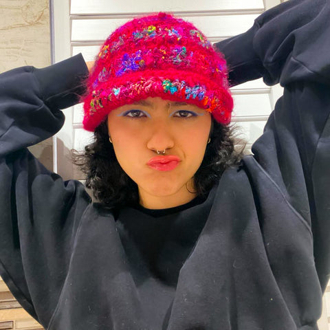 A girl is making a funny face at the camera, wearing a black sweatshirt and a fuzzy warm pink beanie.