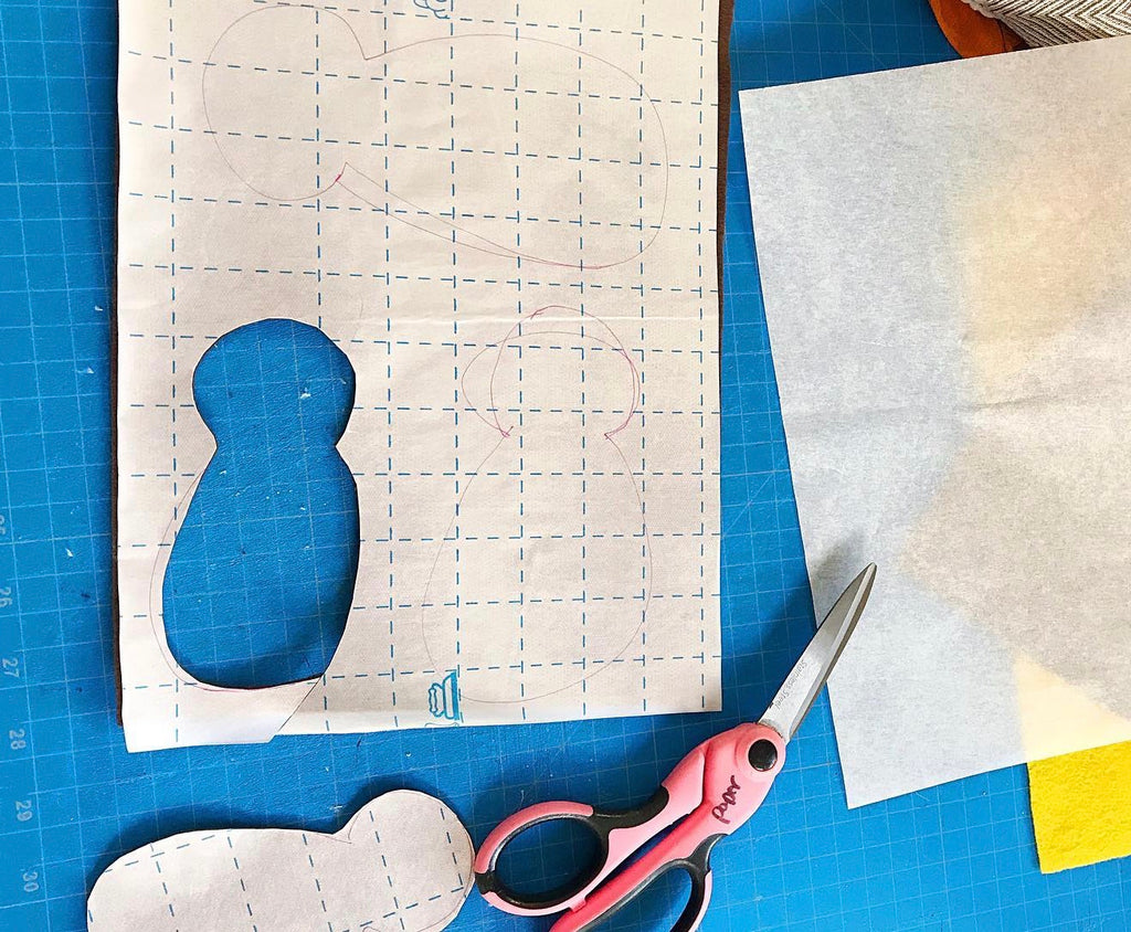 outline of a turkey body cut from a white gridded paper, sitting next to scissors on a blue background