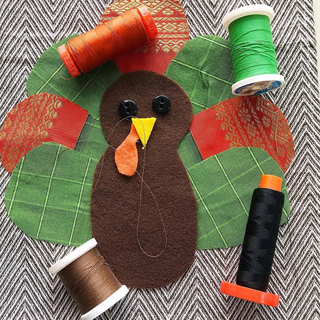 Fabric turkey pieces arranged on a brown hand towel with 4 spools of thread
