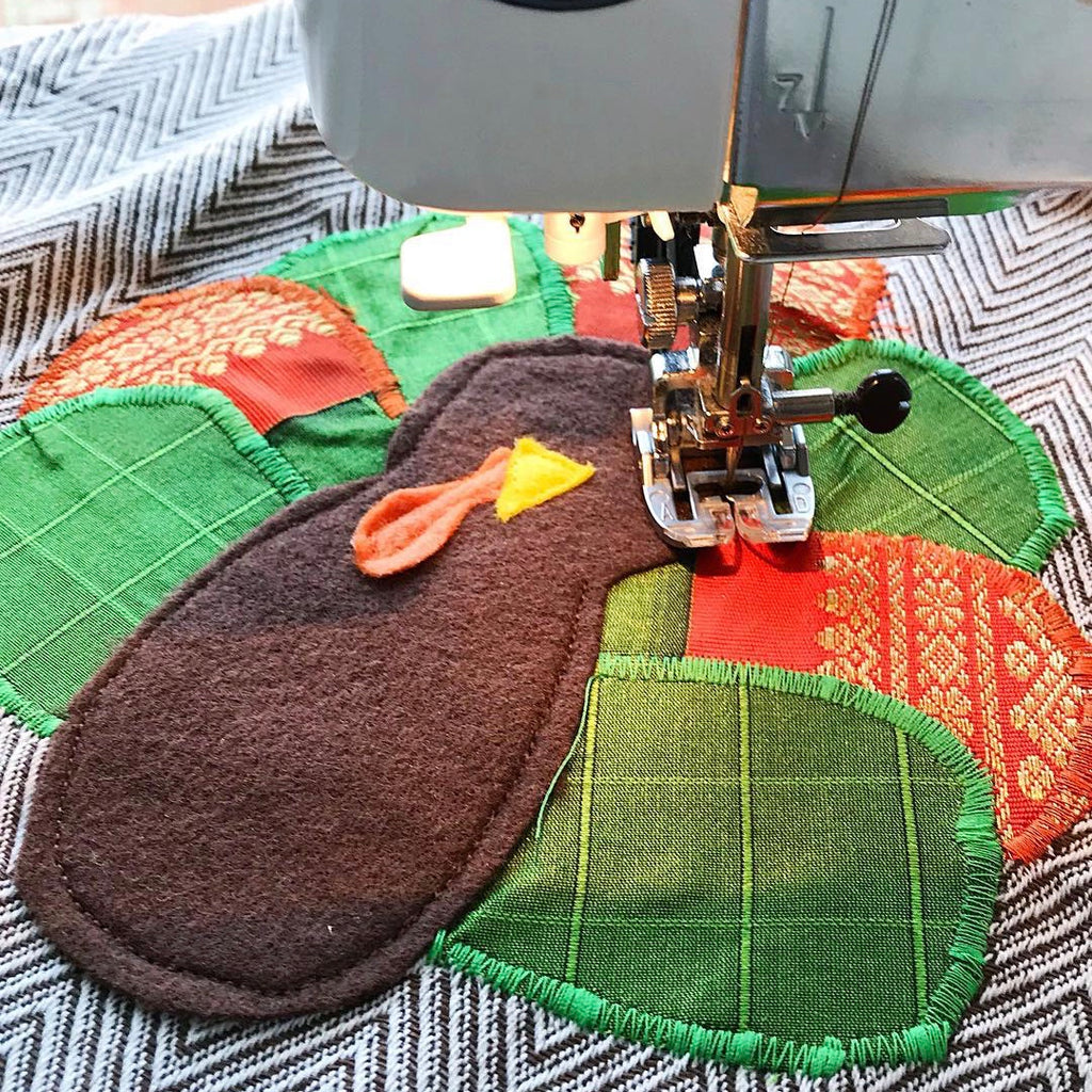 Applique turkey on a hand towel sitting under a sewing machine needle