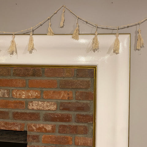 The ghost tassel garland is hung on the wall against a white and brick fireplace, perfect for a spooky halloween night.