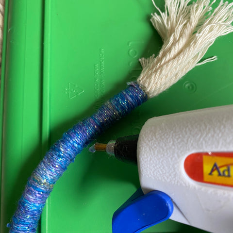 On a green plastic background, a white hot glue gun is squeezing glue out onto the inside of one of our arches.