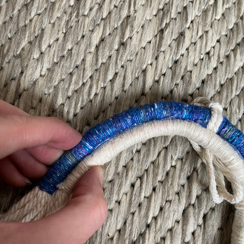 On a tan rug, a sparkly blue yarn wrapped arch is being glued and pressed against a white yarn wrapped arch.