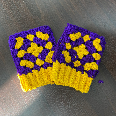 A pair of purple and yellow granny square gloves are laid out on a dark wooden table.