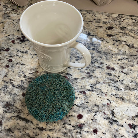 A white Irish cup on a white and black marble countertop. Next to the cup is a blue hemp crochet coaster. 