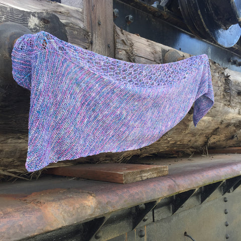 A purple and blue lace weight shawl is stretched out across a wooden display.