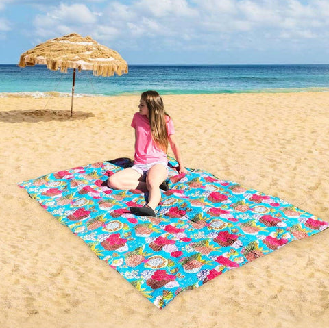 A thin woman with brown hair and a pink shirt is laying on a blue kantha quilt on the beach. Behind her, is a straw umbrella and the blue ocean.