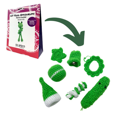 A frog amigurumi kit with a green arrow pointing towards Christmas ornaments in the shape of a pickle, a wreath, an ornament, a star, a coil, a hat, and a bell made out of white and green yarn.