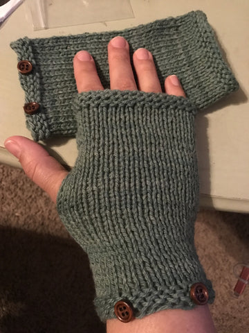 Woman's hand wearing a green fingerless knit glove on top of a matching folded one on a white background