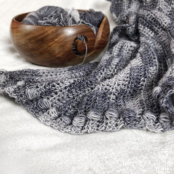 Gray crochet project with wooden yarn bowl on a white background