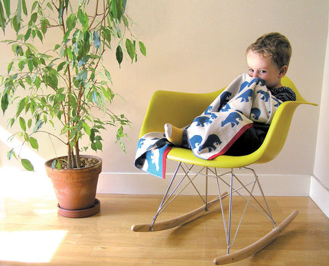 A toddler is sitting on a modern lime green chair with a white, blue, and red blanket wrapped around him.
