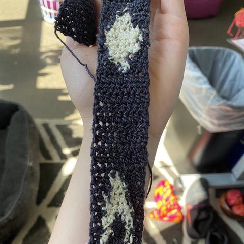 A hand holding a stripe of black yarn, where white yarn has been added to create moon shapes.