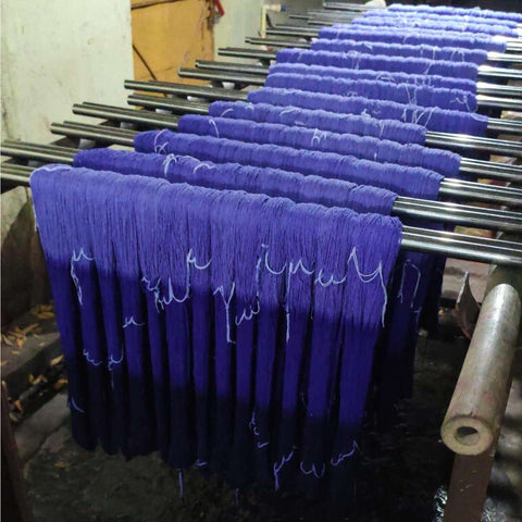Dozens of hanks of purple ombre yarn are being dyed and hung on metal racks.
