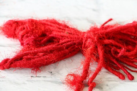 Large knotted strands of red yarn on a white surface