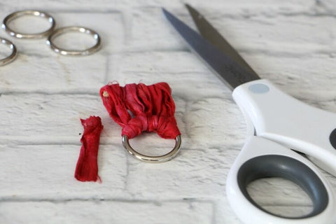 a pair of scissors, a small wooden dowel, and red yarn tied to a metal ring on a white surface