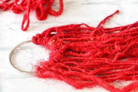 Metal ring with several strands of red yarn hanging from the bottom all sitting on a white surface