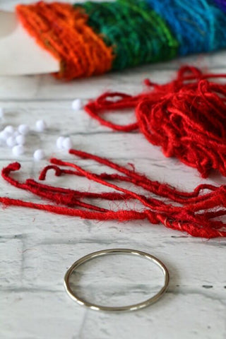 Close up of a yarn sample card, a metal ring, and red yarn strewn on a white surface