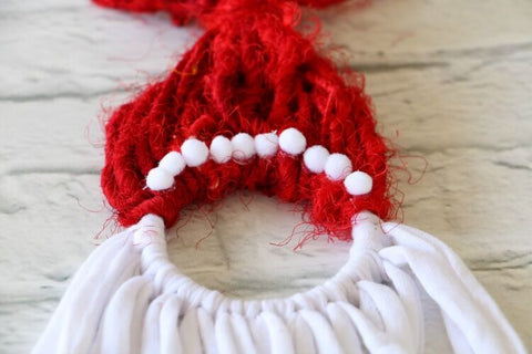 Close up of handmade santa necklace with supplies on a white surface