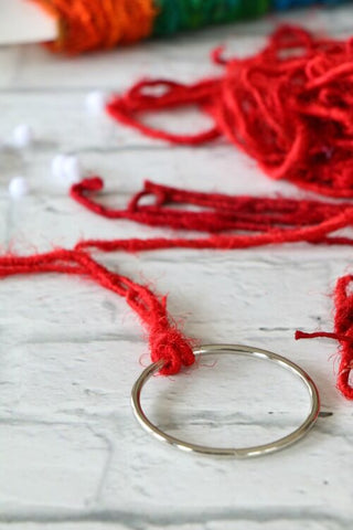 Metal ring with red yarn tied onto it and yarn sample cards on a white surface