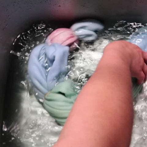 A hand is swishing around a tied tie-dyed shirt in water, rinsing the dye out of the fabric
