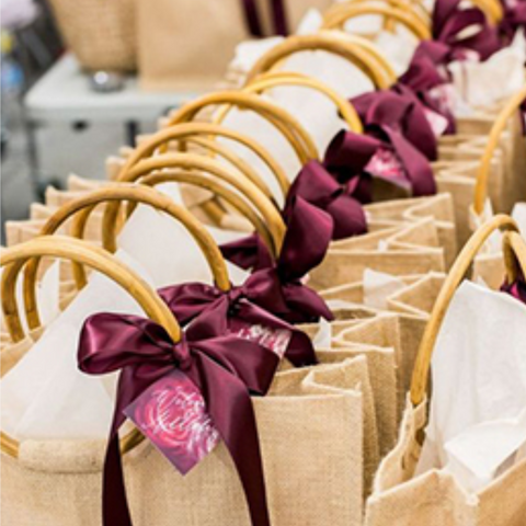 A line of burlap favor bags with deep wine ribbons attached to their handles are neatly lined up to be snagged.