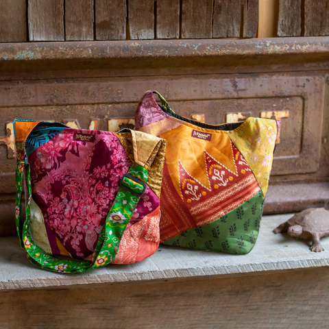 Two one-of-a-kind recycled sari silk purses are sitting on a bench.