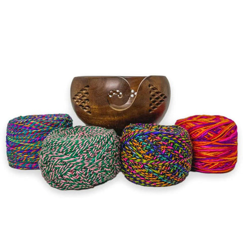 A gorgeous wooden yarn bowl is resting ontop of colorful skeins of sport weight twist yarn.