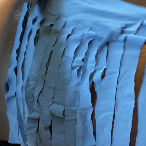 A blue square of tshirt fabric, cut into thin one inch strips.