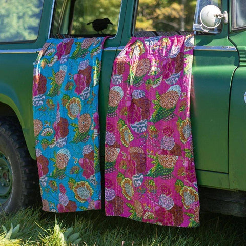 An old green truck has two kantha quilts hanging from the open windows.