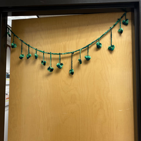 A wooden door is mostly closed, with a sliver of bright light peeping through the crack. A green heart garland hands in a grand swoop just below the top of the door.