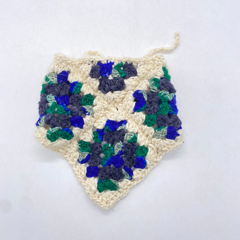 A granny square bandana made of white, green, blue, and black worsted weight yarn is folded up and laid out on a white background.