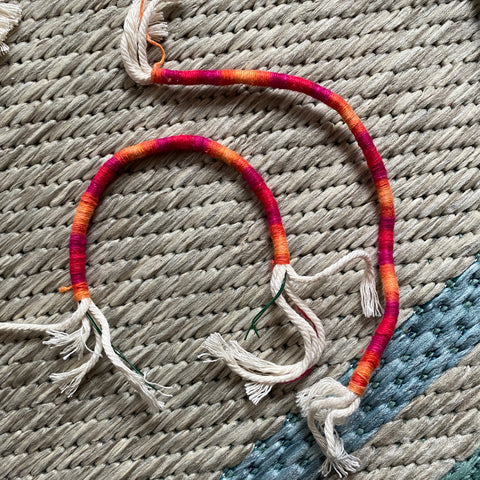 On a tan rug, two different yarn wrapped macrame bundles lay. The one with wire is in an arch, while the one without wire is laying in a floppy line.
