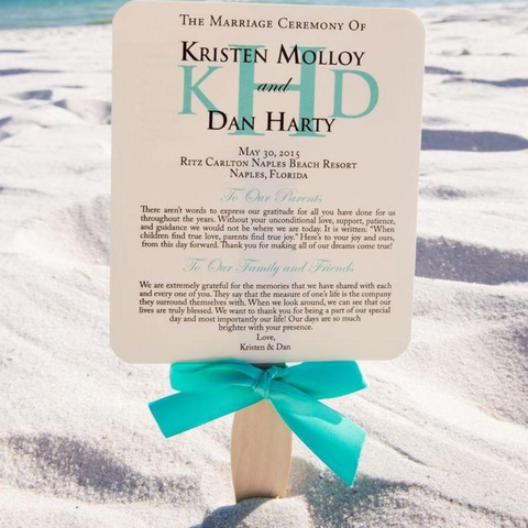 A wedding program is stuck into the white sand of the back by its handle, a bright blue ribbon wrapped around the bottom of the program.