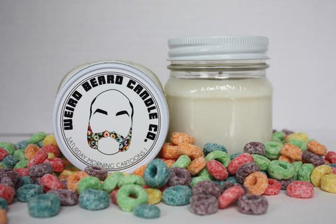 White jar candle with lid that reads 'Weird Beard Candle Co' sitting in a pile of fruit loops on a white surface