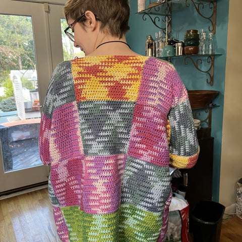 A person with short hair is facing away from the camera, showing off the back of the worsted weight patchwork cardigan.