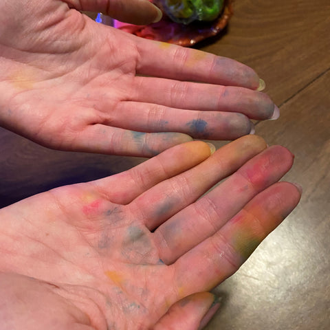 A pair of hands are outstretched, showing the different colors of dye that has stained the skin.