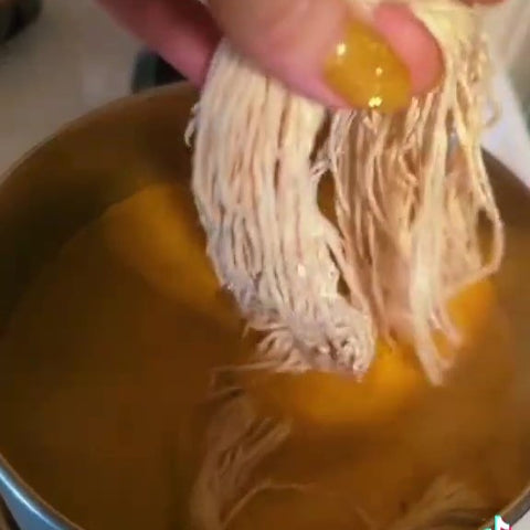 A hand with bright yellow nails is dipping white worsted weight yarn into the turmeric dye in the pot on the stove. 