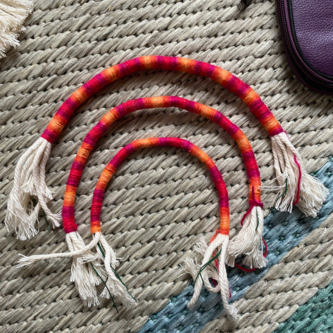 Three different sized macrame rope rainbow arches that are wrapped in red and orange ombre yarn.